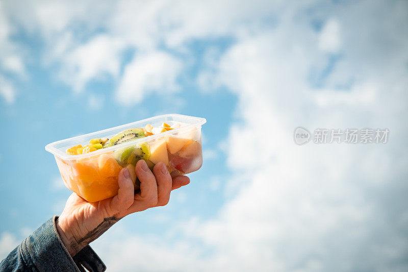 Hands hold plastic container with fruits.